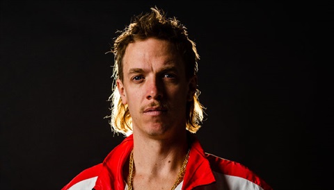 head shot image of male Caucasian with blonde mullet hairstyle and red and white jacket on