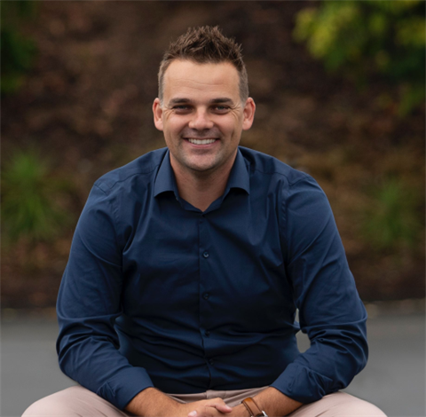 Close up of man wearing a blue shirt and sitting in front of trees