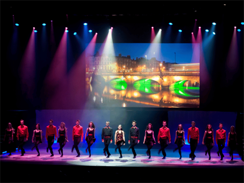 Stage with blue and purple lights shining down on dancers.Projector screen behind depicts image of bridge. 